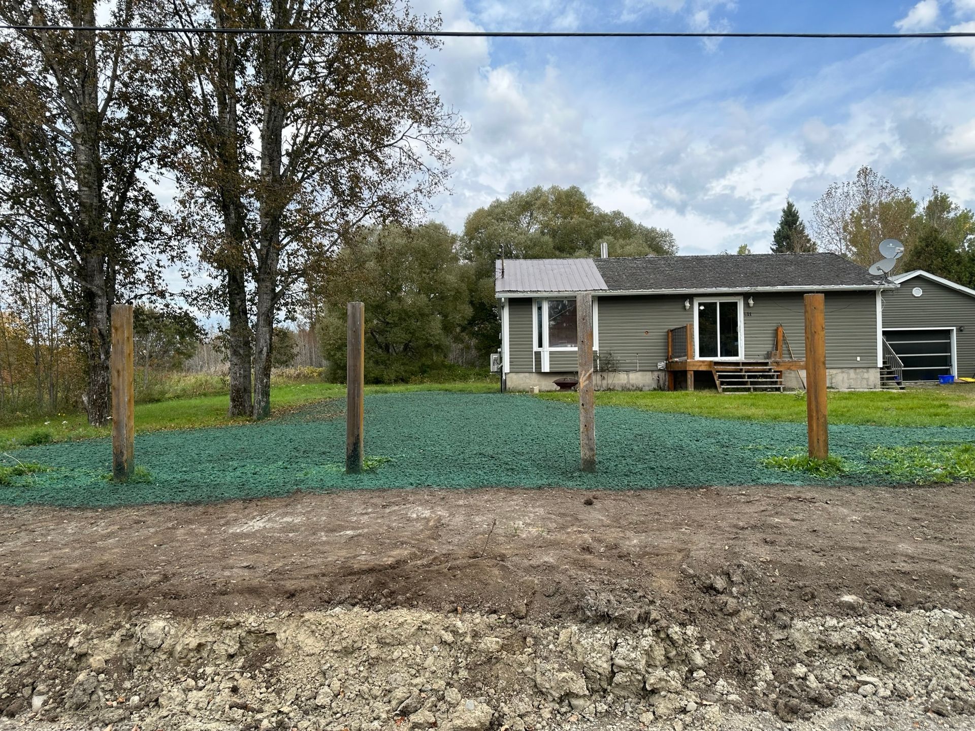Une propriété résidentielle avec une petite maison, un couvre-sol végétalisé et des poteaux en bois à l'avant.