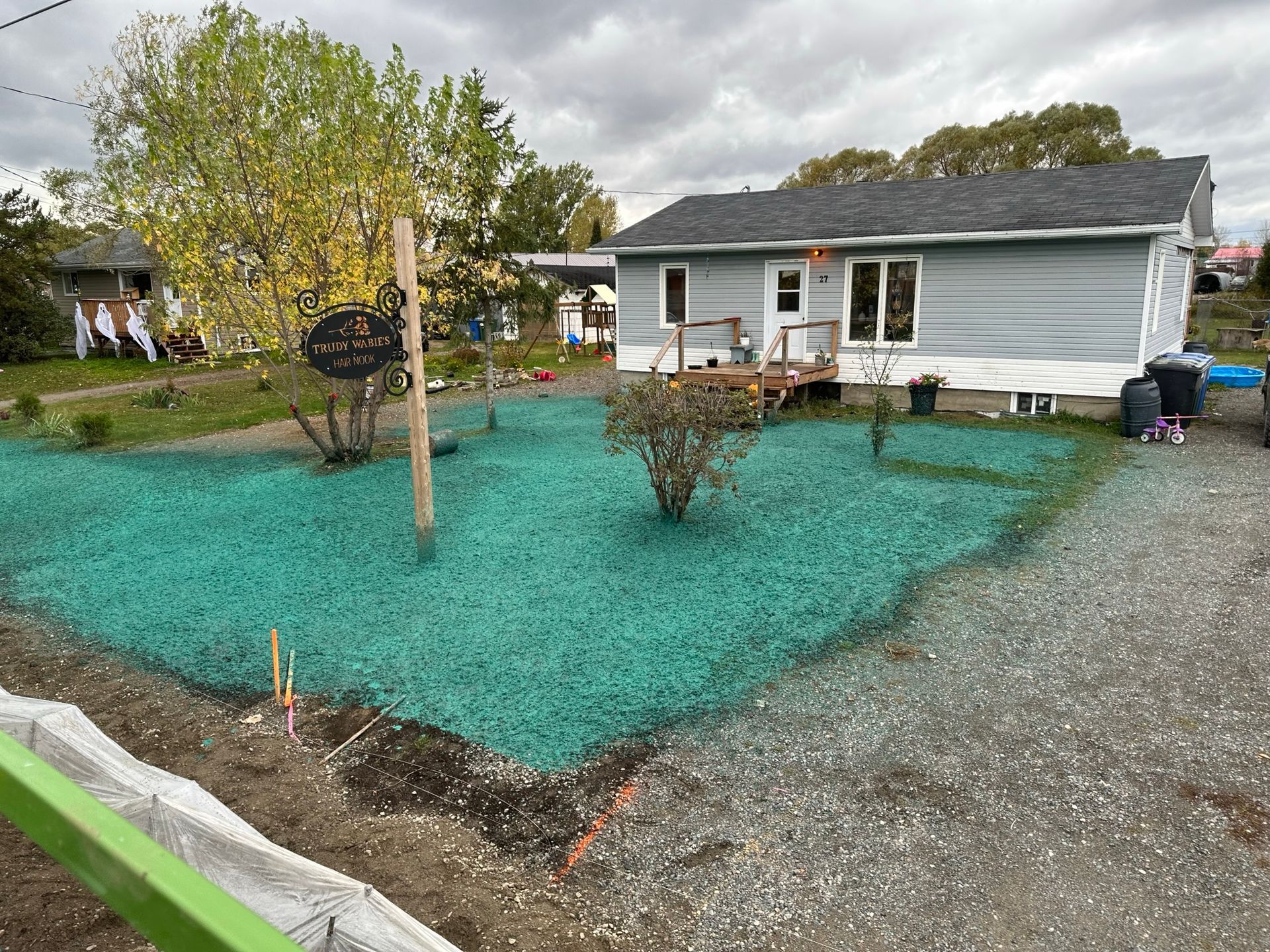 Une maison bleu clair avec un porche couvert se dresse derrière une cour de gravier parsemée d'un gazon hydrosemé d'un vert éclatant.