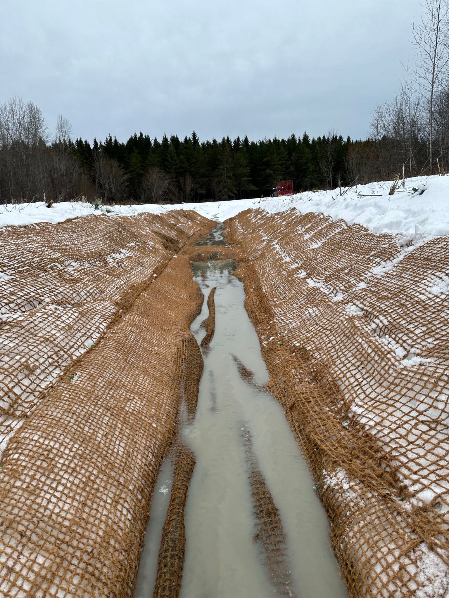 Fossé de drainage enneigé avec des filets bruns sur les côtés, l'eau s'écoulant au centre.