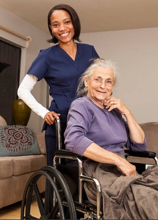 A nurse is standing next to an elderly woman in a wheelchair.