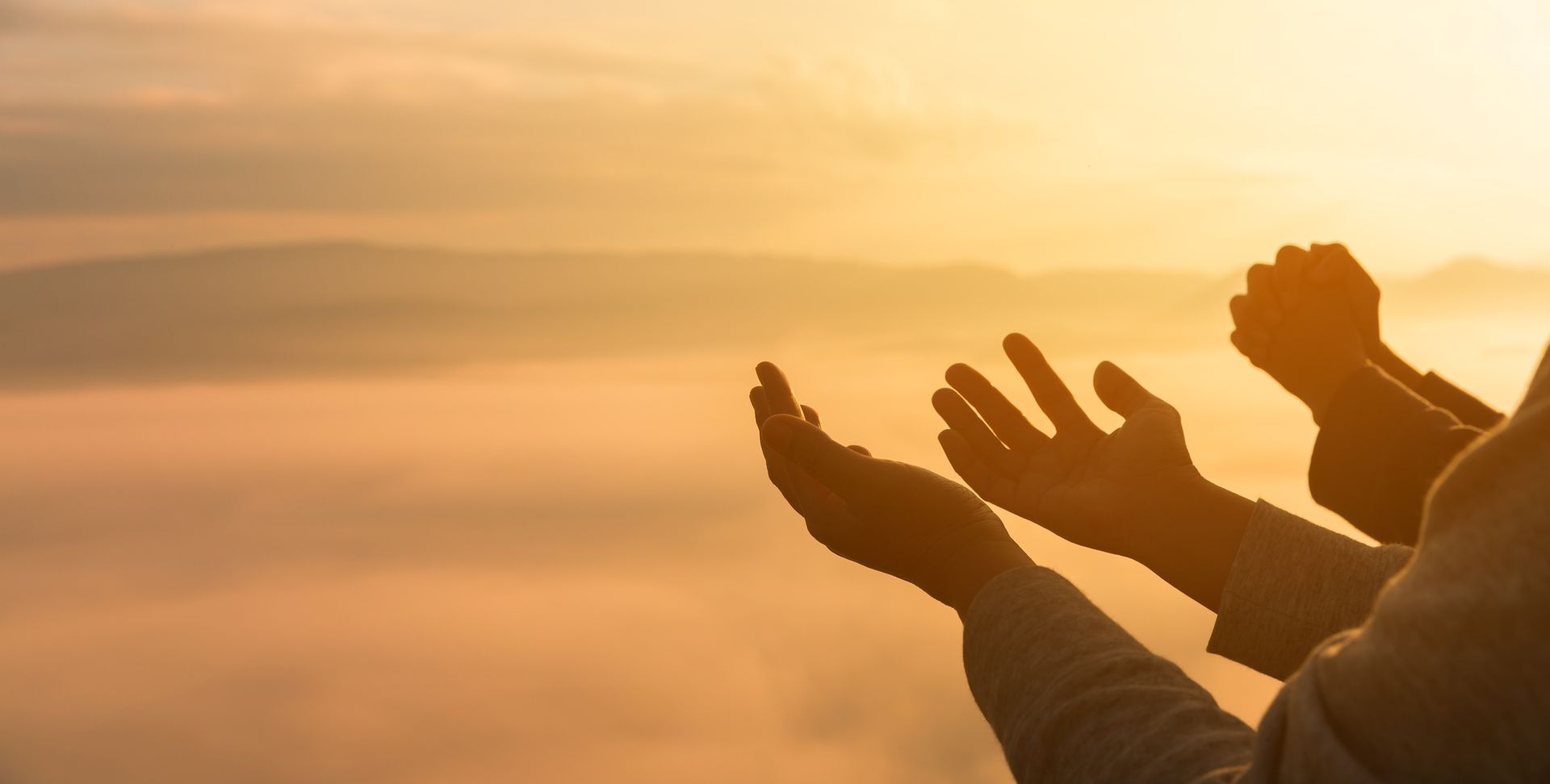 Outstretched hands reaching toward a golden sunrise above a sea of clouds