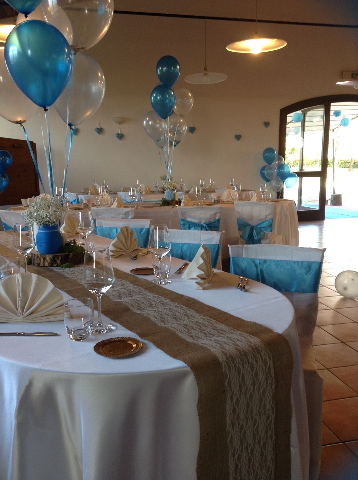 Una stanza con tavoli e sedie decorati con palloncini blu e bianchi