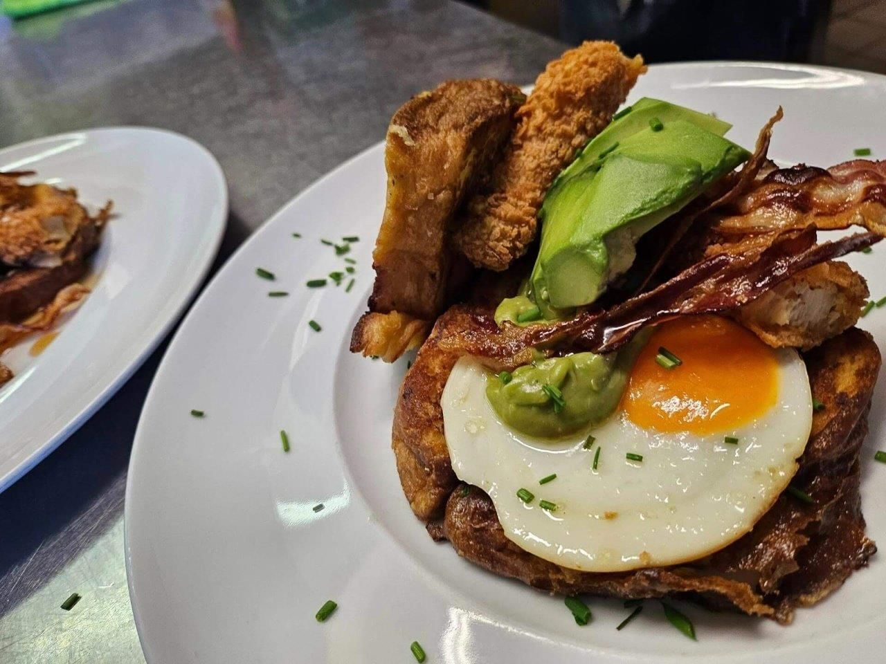 Un piatto bianco con sopra un uovo fritto, bacon e avocado