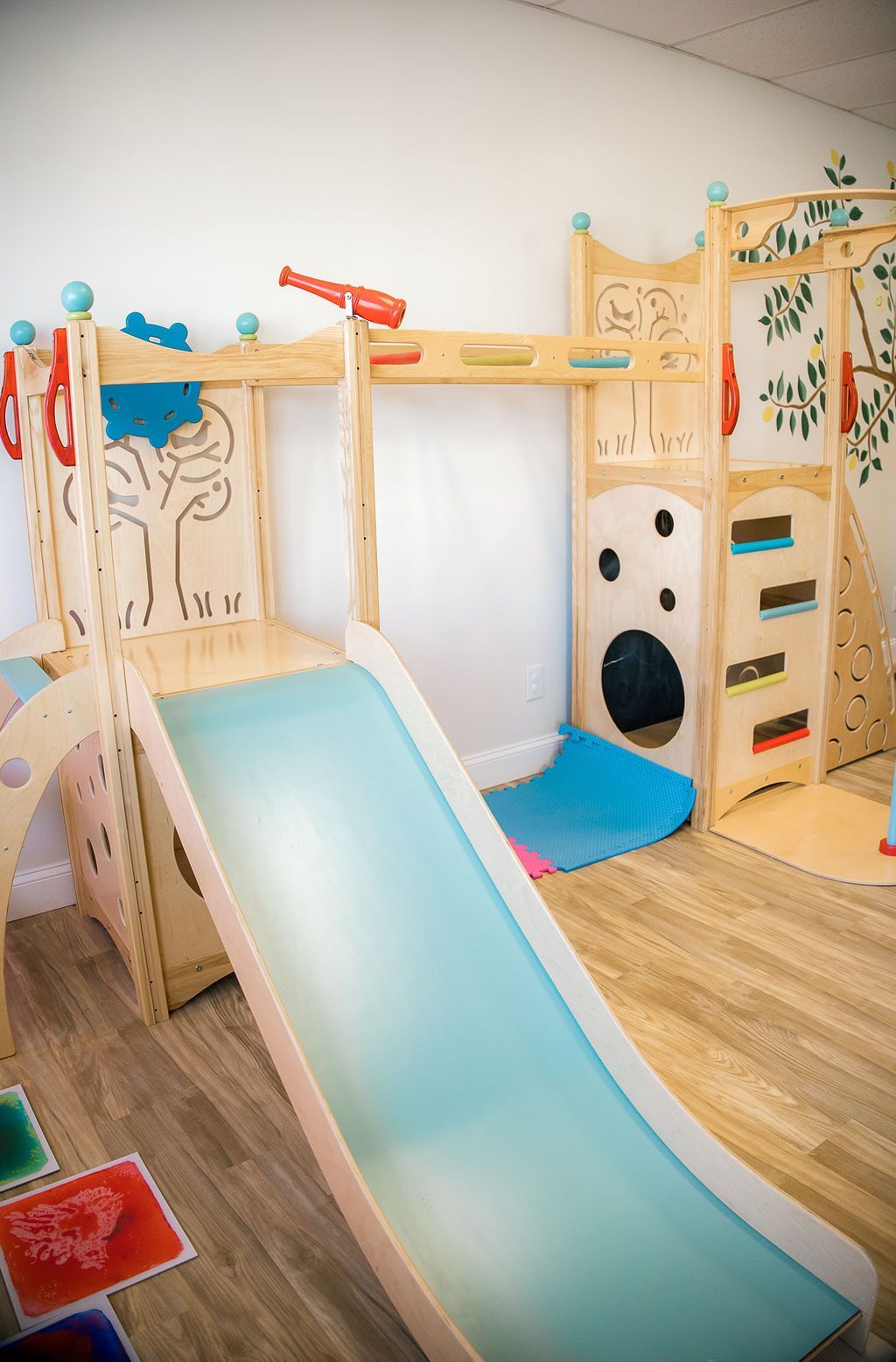 A wooden playset with a slide and climbing wall at The Lemon Lounge Indoor Playground.