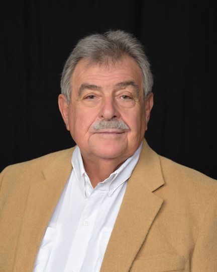 Man with graying hair, mustache, wearing a tan jacket and white shirt.