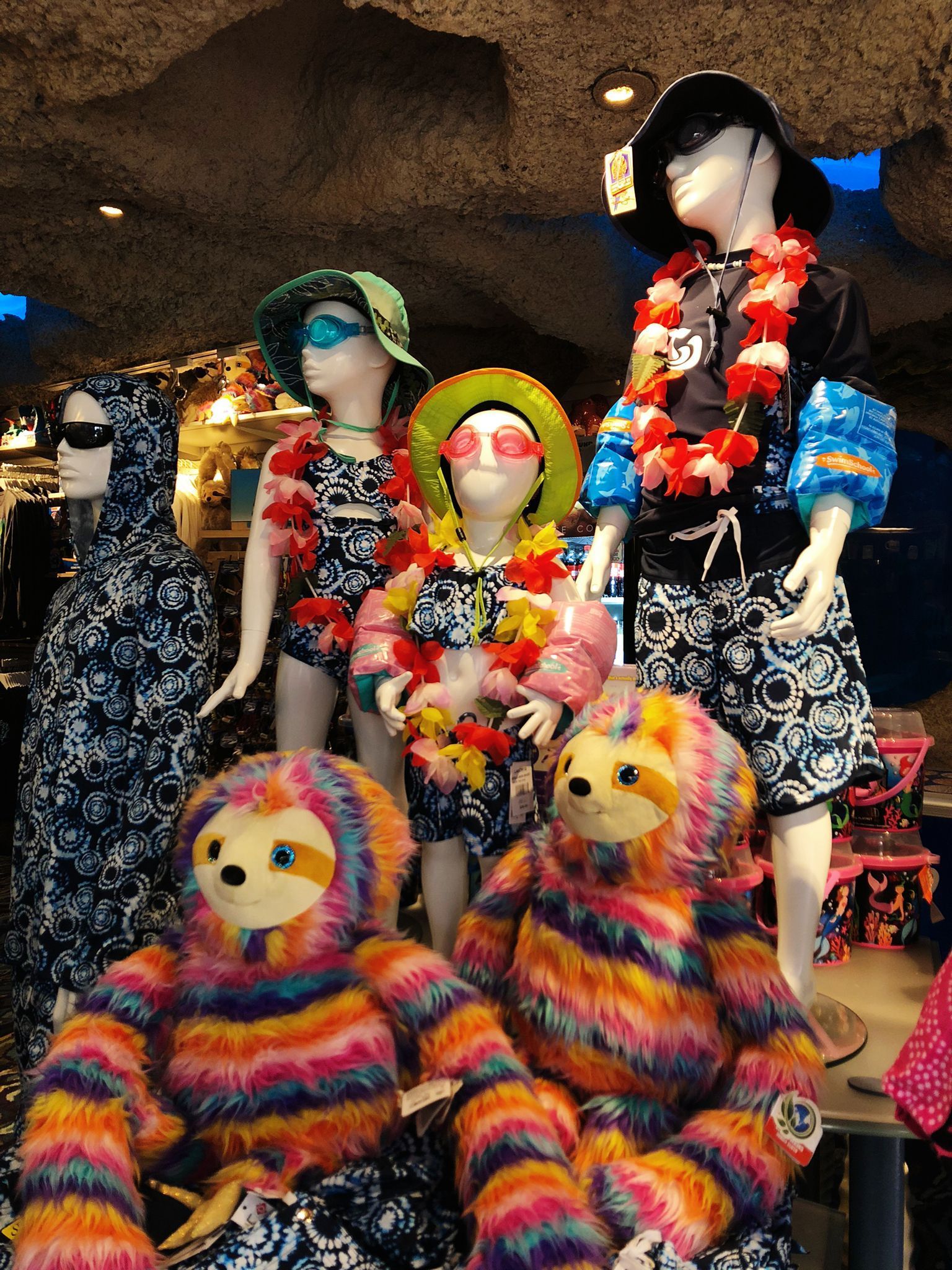 Mannequins and sloth stuffed animals in tropical attire, store display.