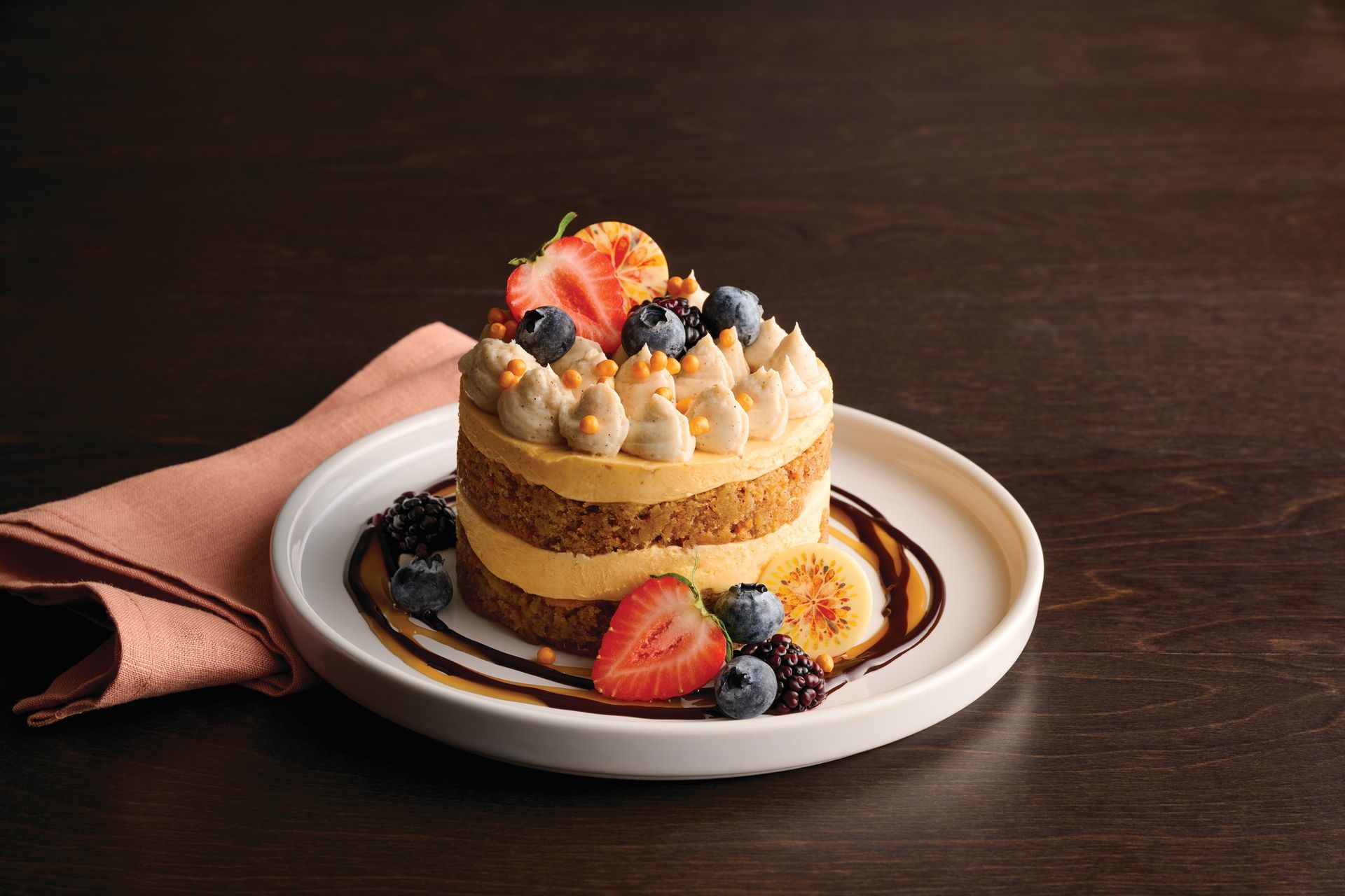 Pumpkin spice cake slice with whipped cream, berries, and sprinkles on a white plate.