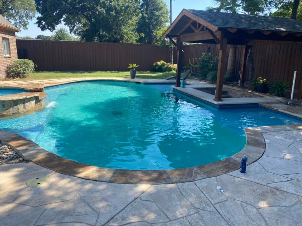 Backyard swimming pool with blue water, stone deck, and covered seating area