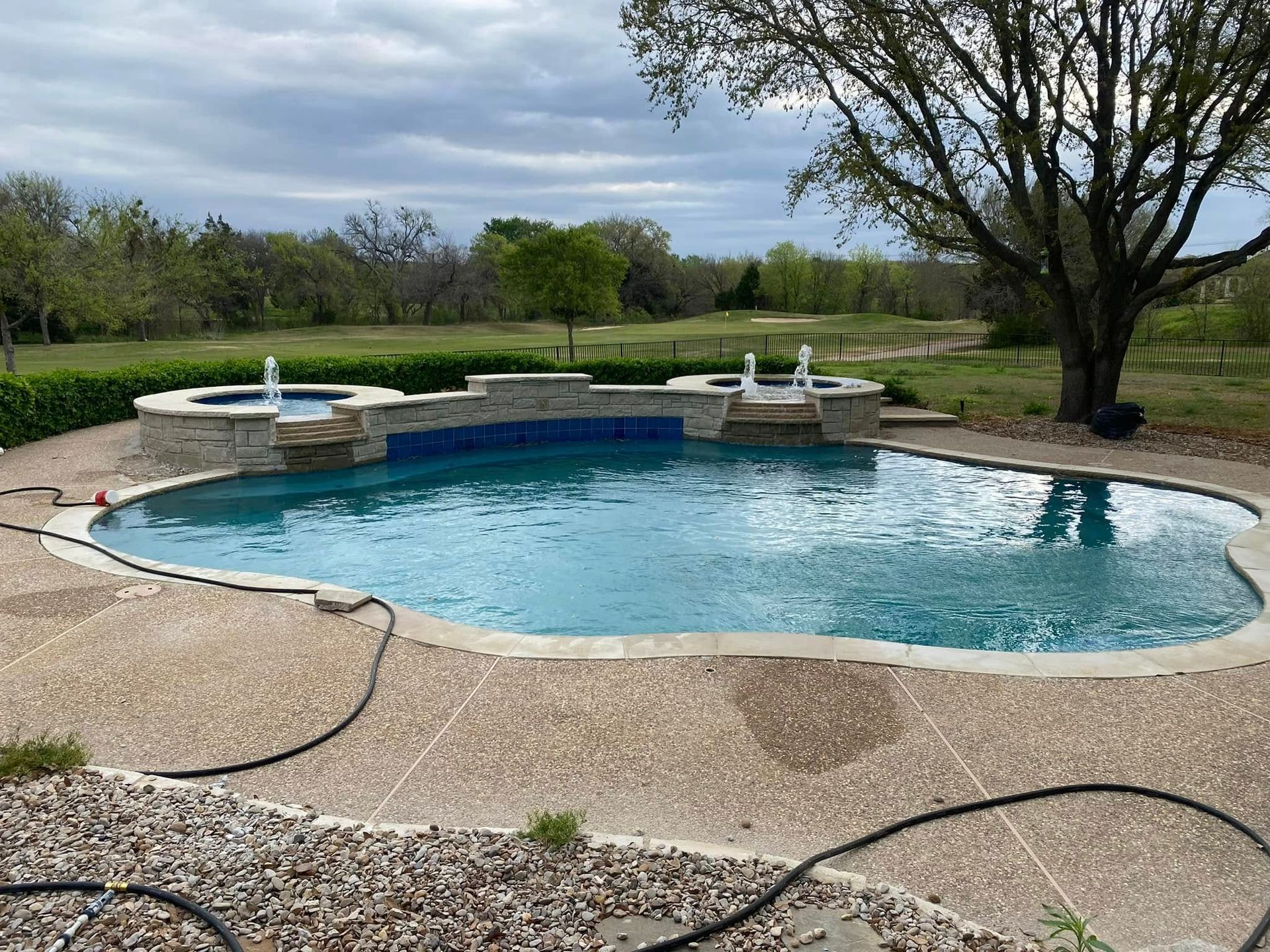 Backyard swimming pool with stone deck, trees, and cloudy sky