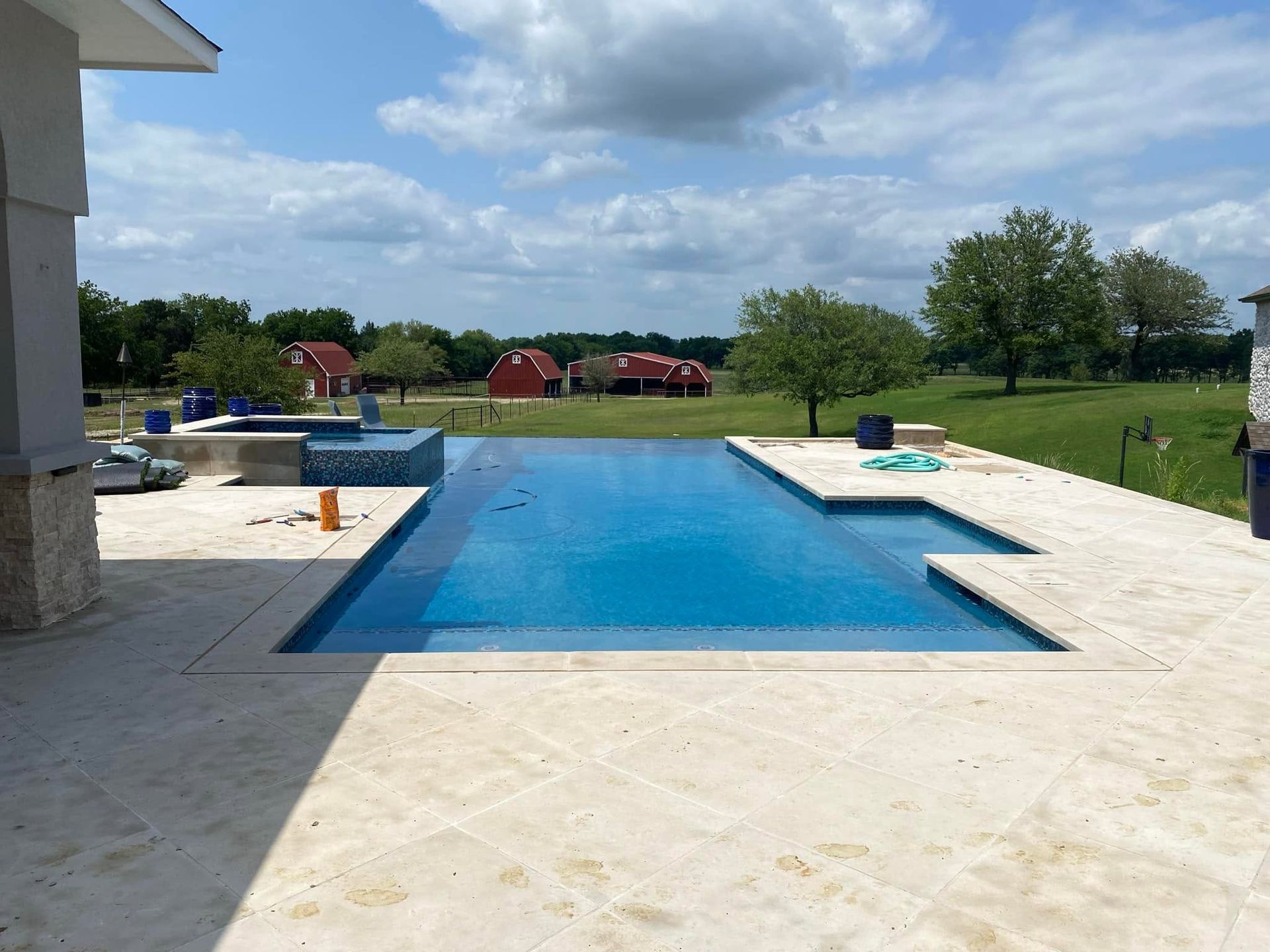 Outdoor swimming pool with blue water, white deck, and grassy landscape under a cloudy sky