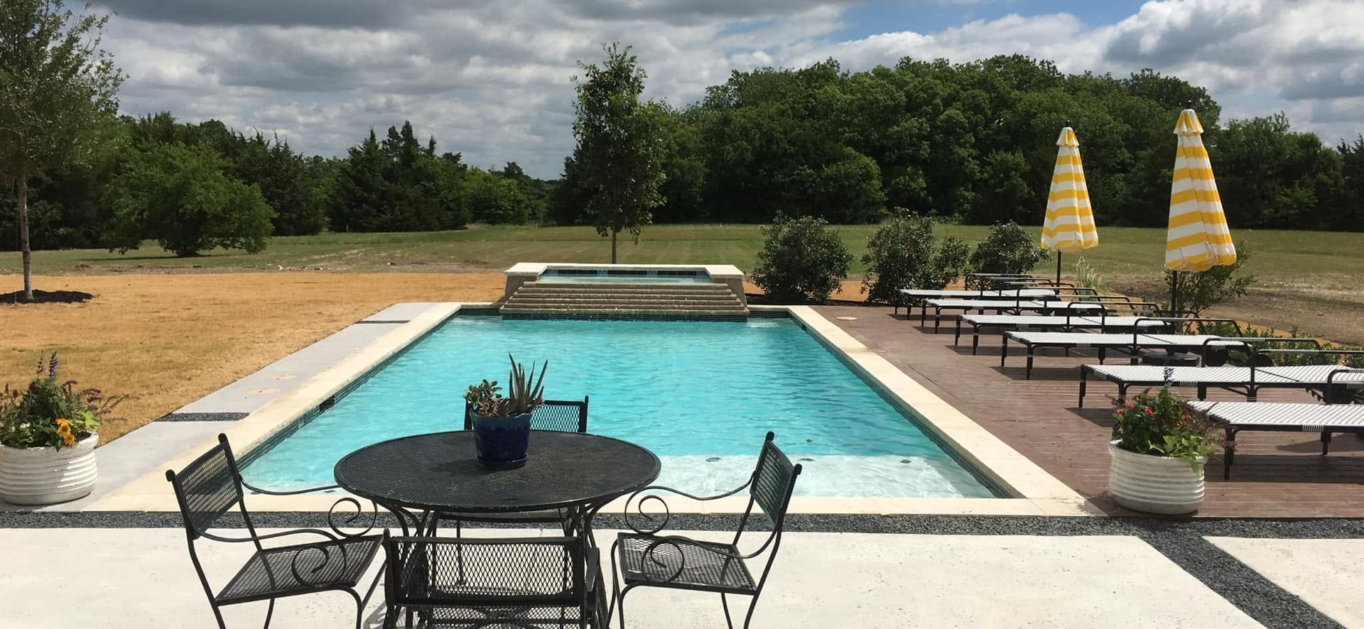 Poolside patio with turquoise pool, black chairs, and yellow umbrellas in a landscaped outdoor setting