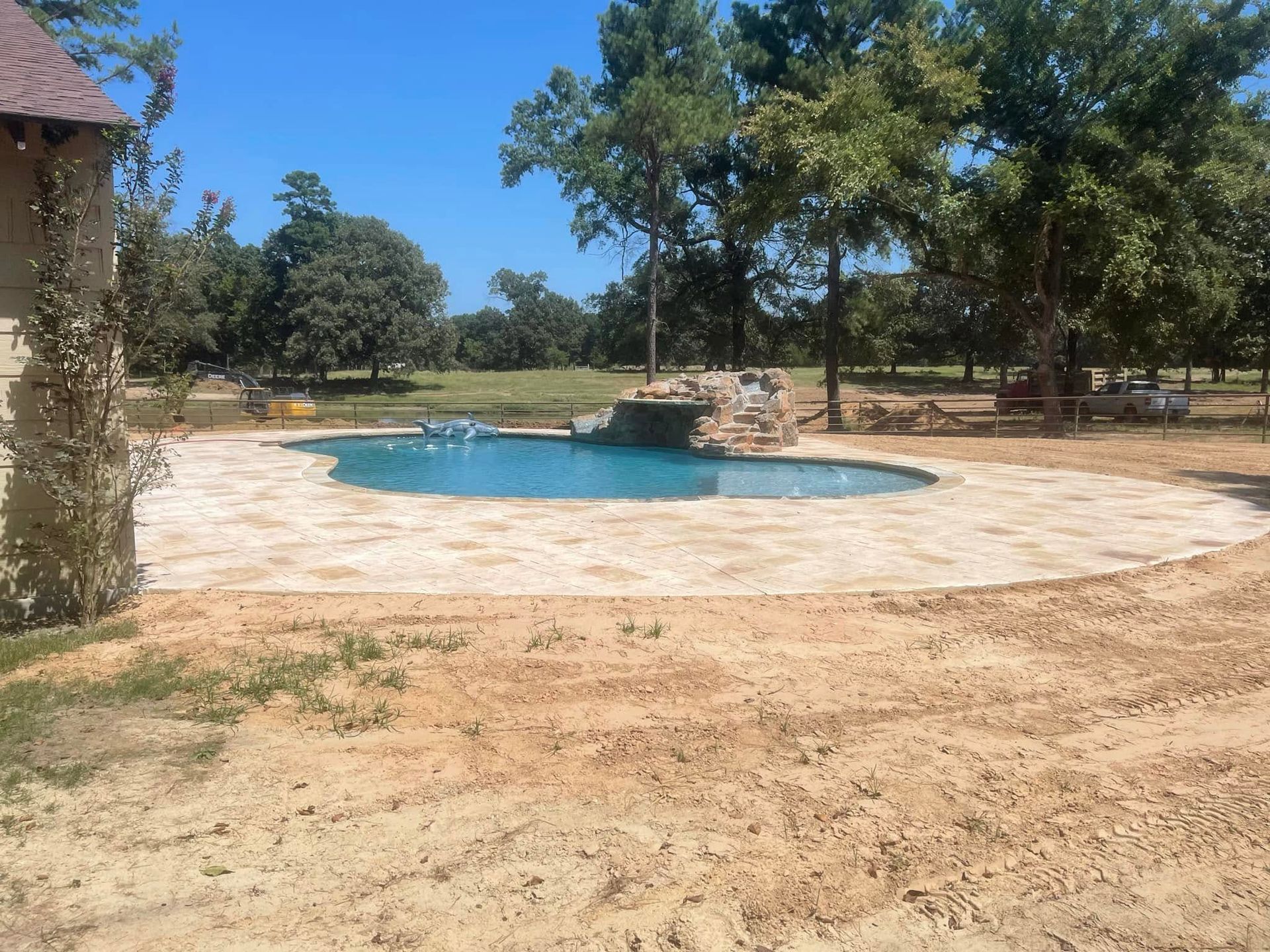 Outdoor stone patio with a small blue pool, surrounded by trees under a clear sky.