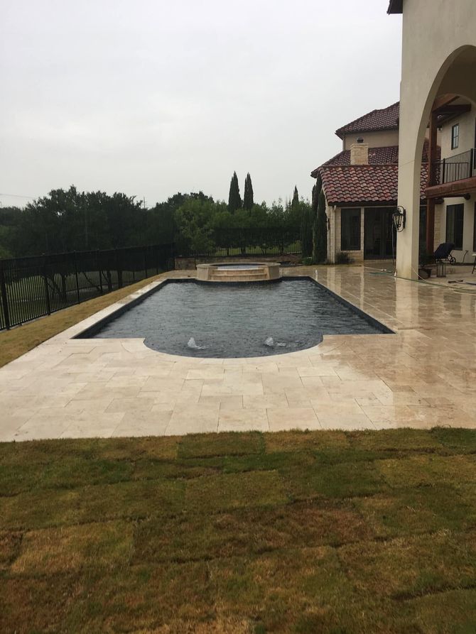 Patio with a narrow rectangular pool beside a house, overlooking a grassy yard and distant trees