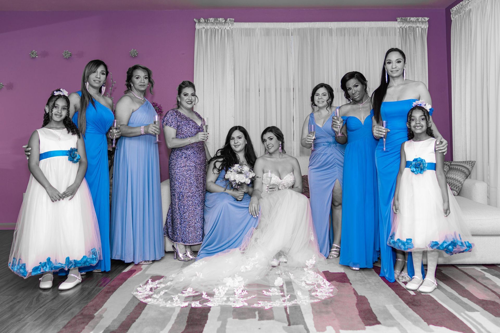 Wedding party posing indoors with a bride in white gown and attendants in blue dresses against a purple wall