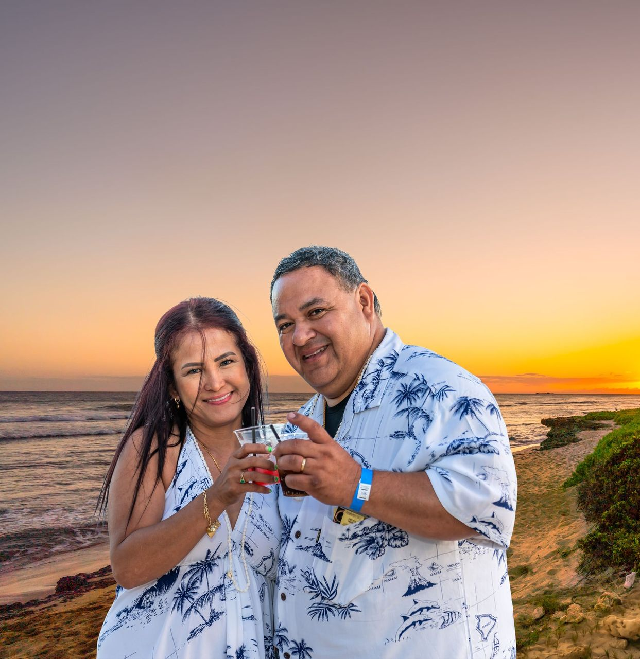 Couple holding drinks at sunset near a tall lighthouse by the coast