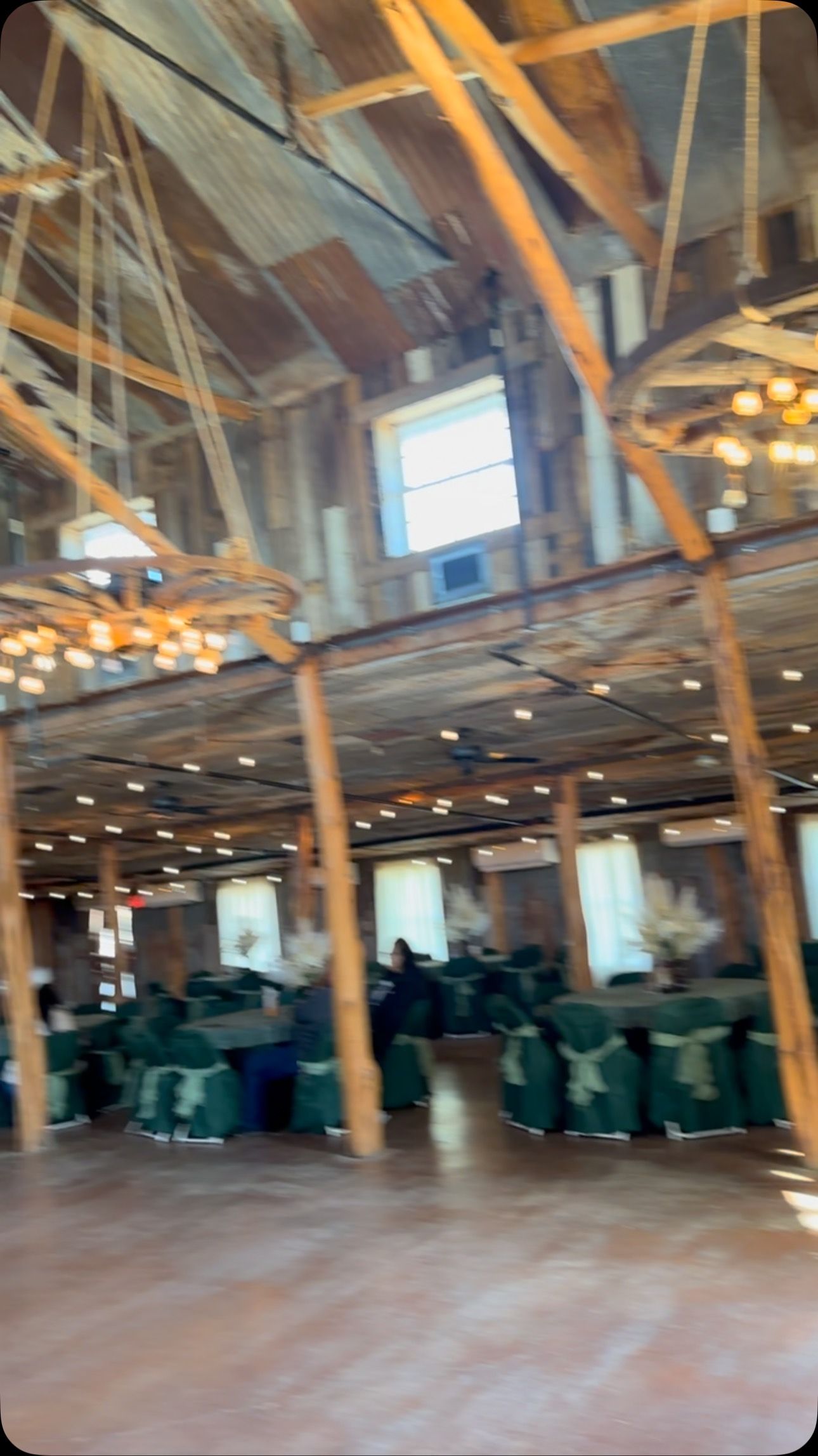 Rustic banquet hall with green-covered tables, wooden beams, and a brightly lit ceiling mural