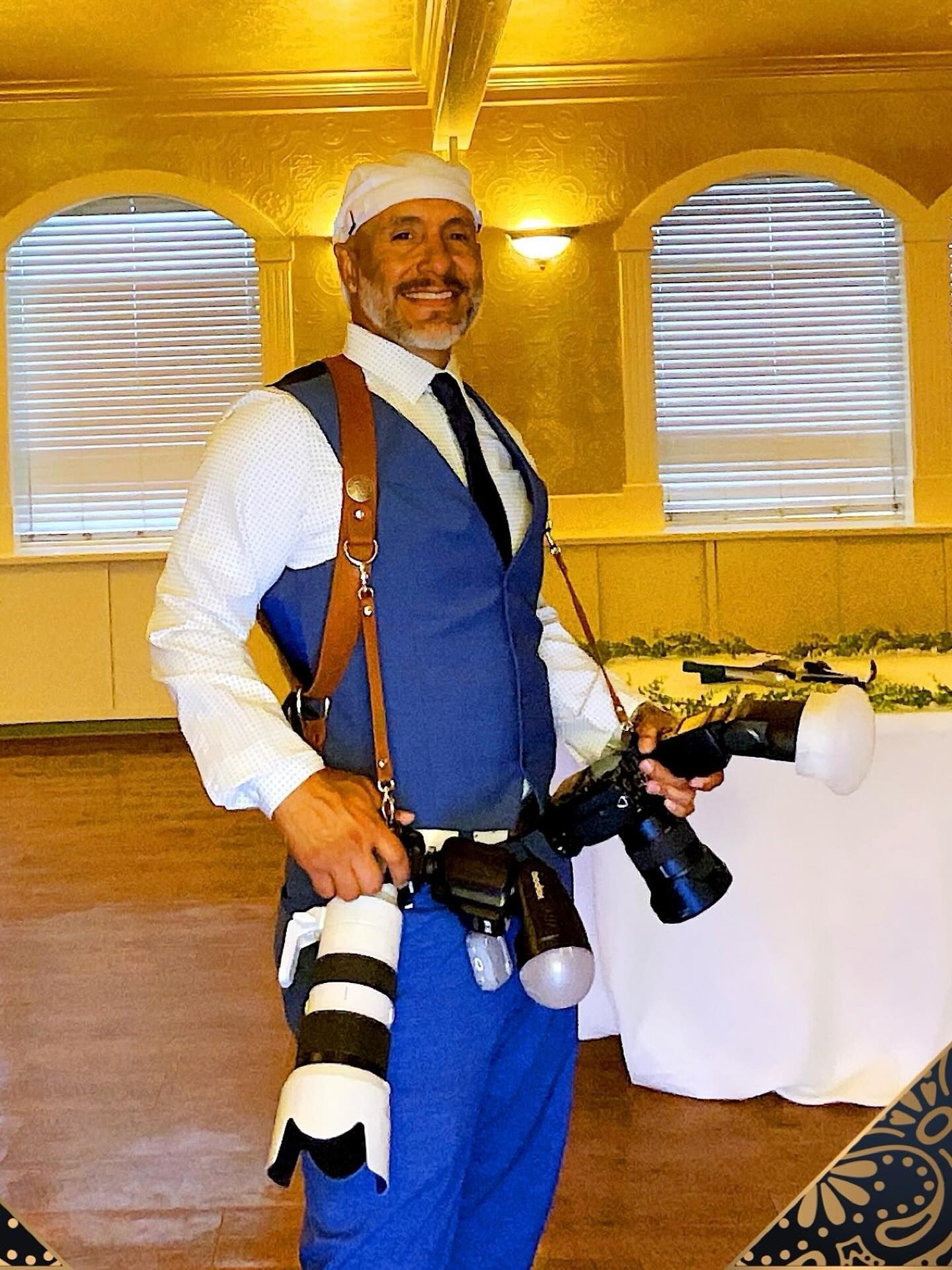 Person in blue vest and white shirt holding camera gear in a warmly lit room with arched windows