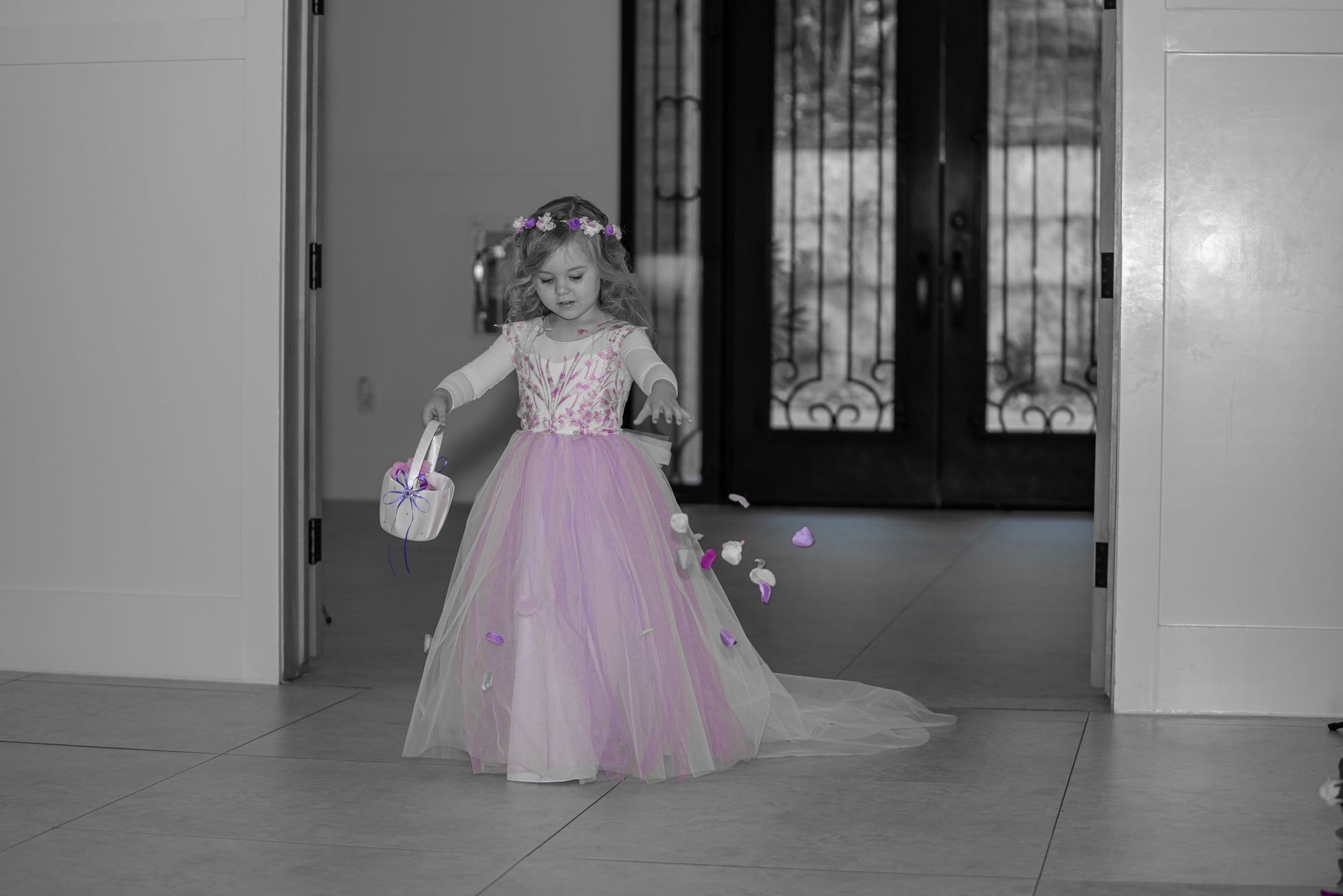 Child in a pink dress holding a basket, standing in a hallway with doors behind her.
