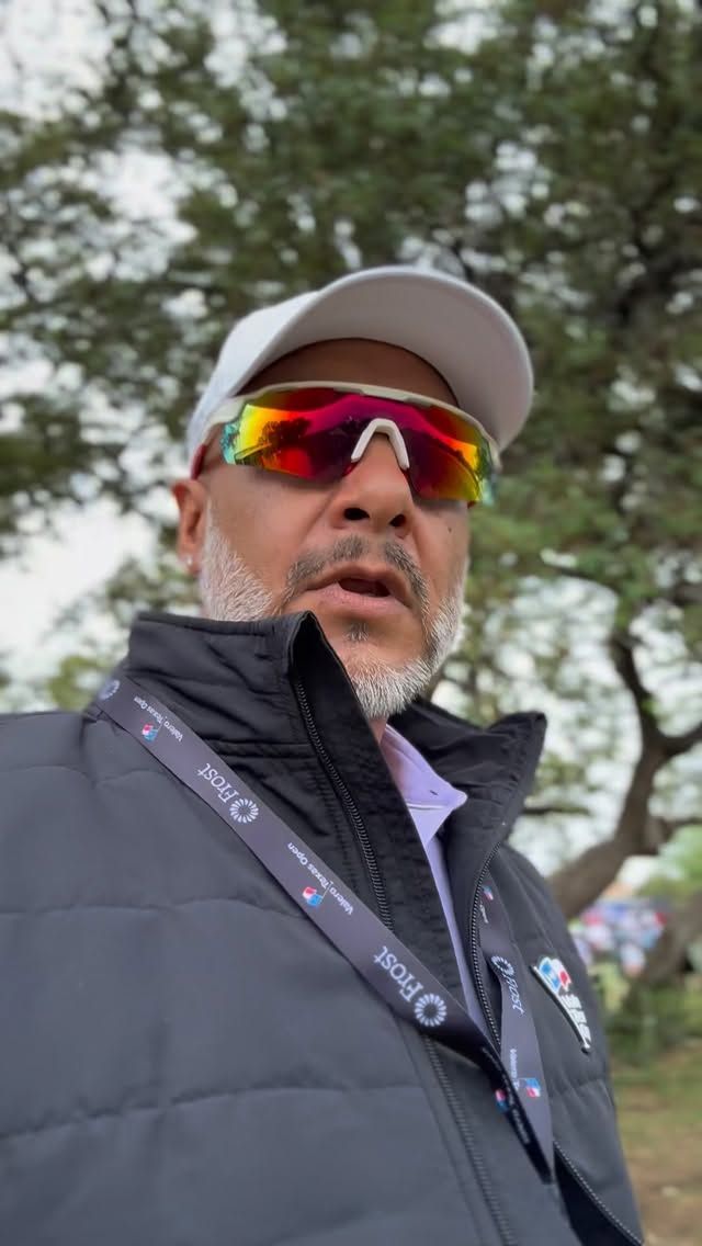 Man wearing a white cap and mirrored sunglasses outdoors, with trees in the background.