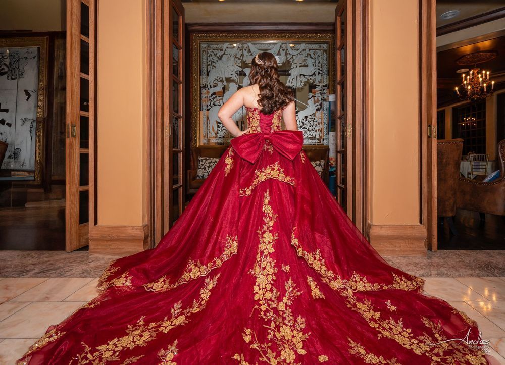 Woman in a red-and-gold gown standing in a grand hallway, seen from behind.