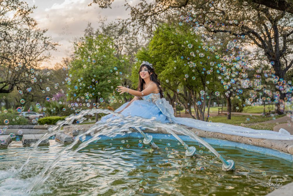 Woman in a blue dress seated on a fountain, splashing water in a garden at sunset