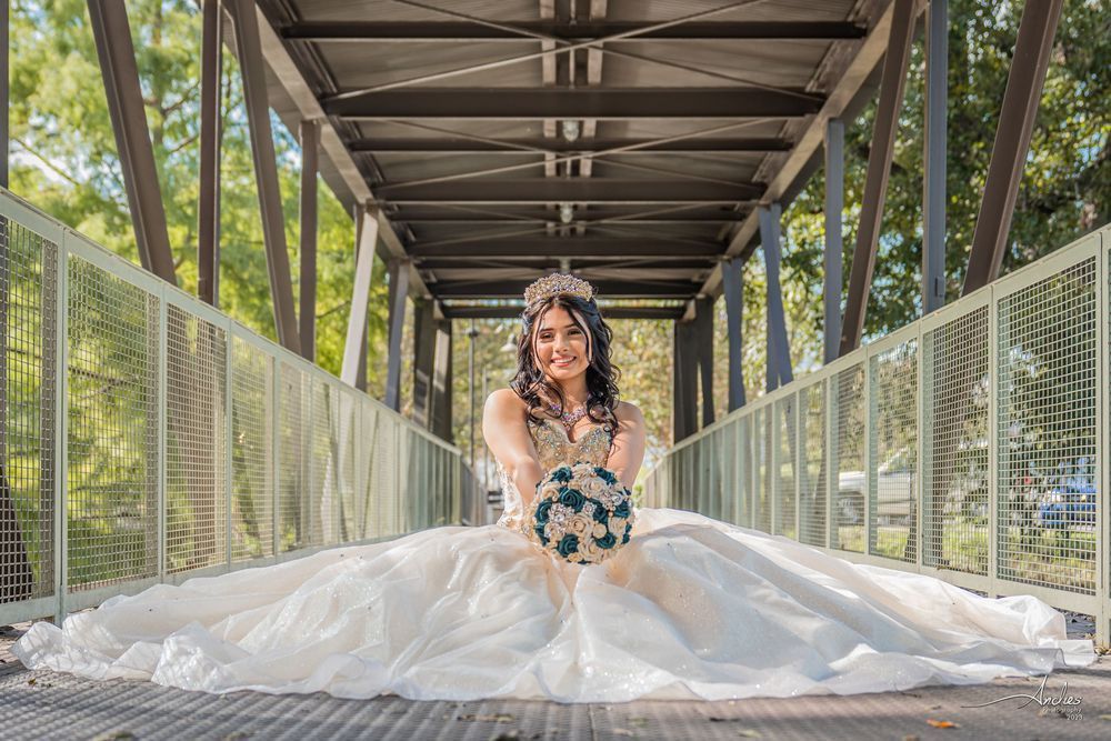Woman in a white gown sitting on a pedestrian bridge, centered under a metal canopy.