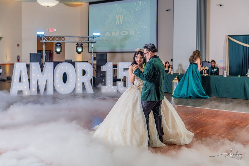 Wedding couple dancing amid low fog with large “AMOR 1.0” letters in a reception hall