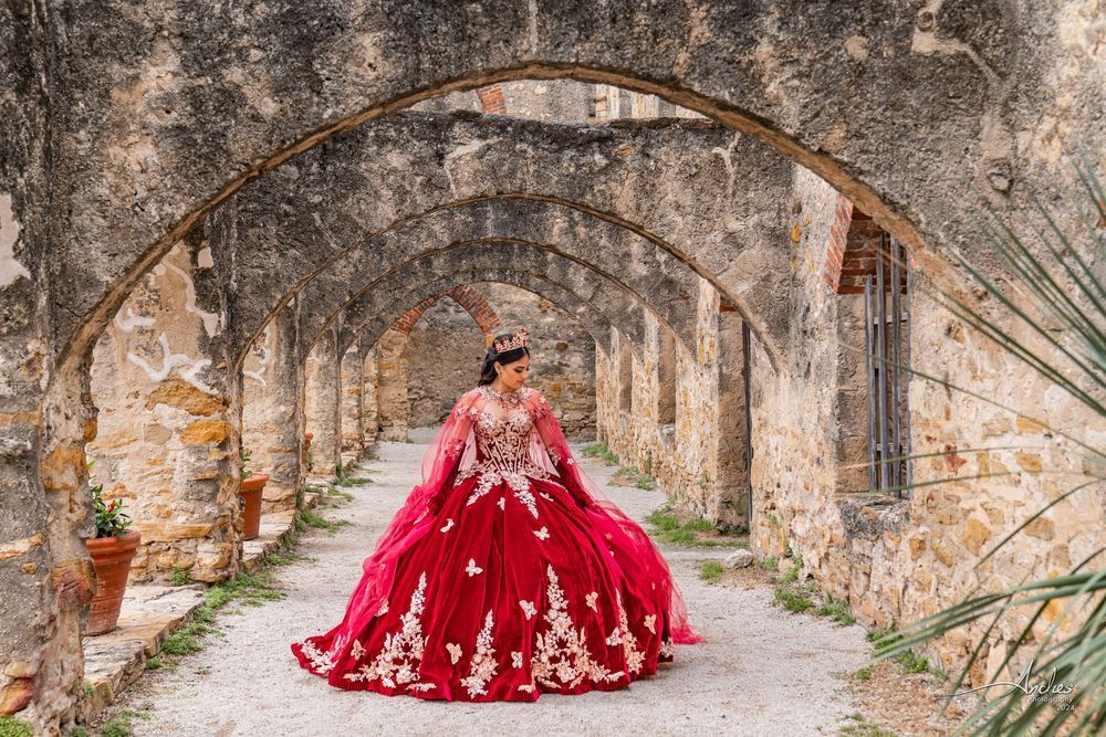 Woman in a bright red gown standing in a stone archway corridor