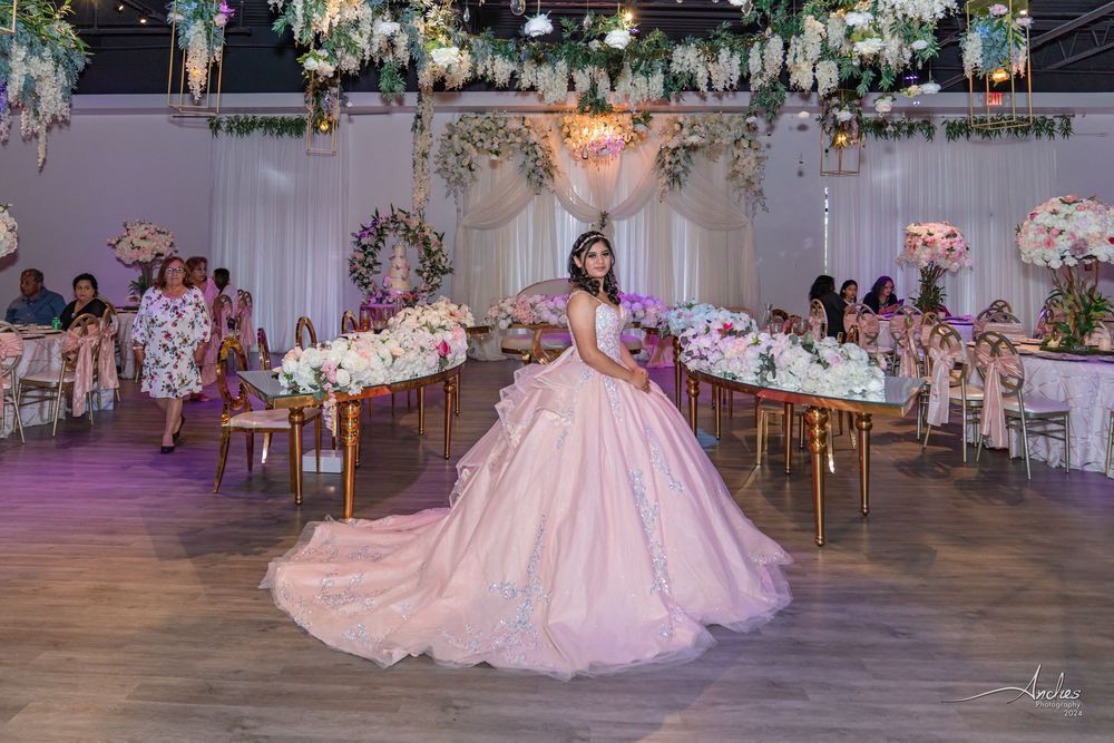 Bride in a pink gown posing in a decorated wedding hall with floral tables and string lights