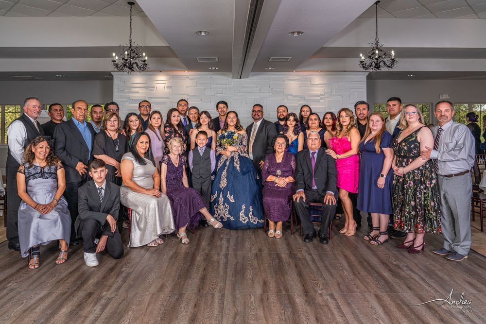 Large group posing for a formal event in a banquet hall, with women in dresses and men in suits.
