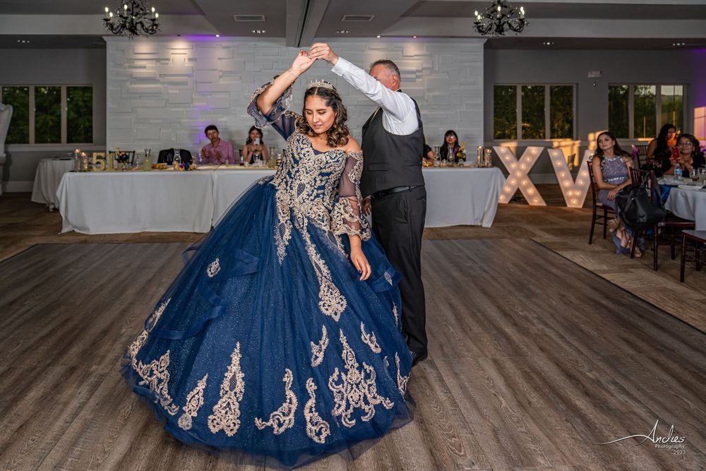 Couple dancing at a formal reception, woman in a navy blue gown with gold embroidery, man in a vest behind her