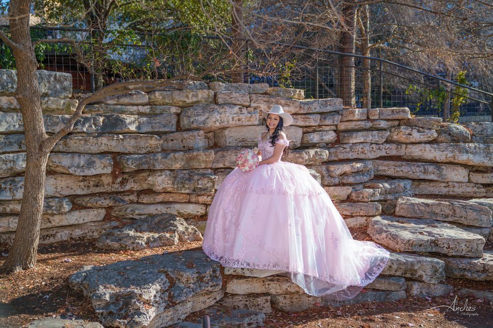 Woman in a pink ballgown posing on stone steps outdoors in a wooded garden