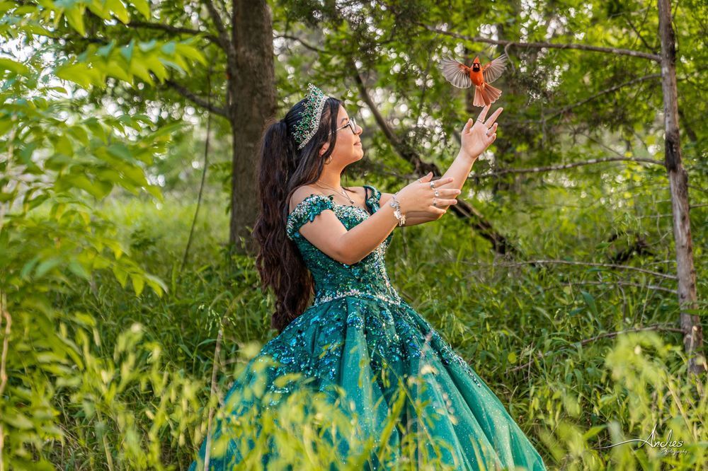 Woman in a green dress reaching toward a butterfly in a lush garden.