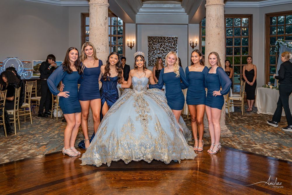 Bride in blue-and-gold gown with five bridesmaids in blue dresses at a formal indoor reception