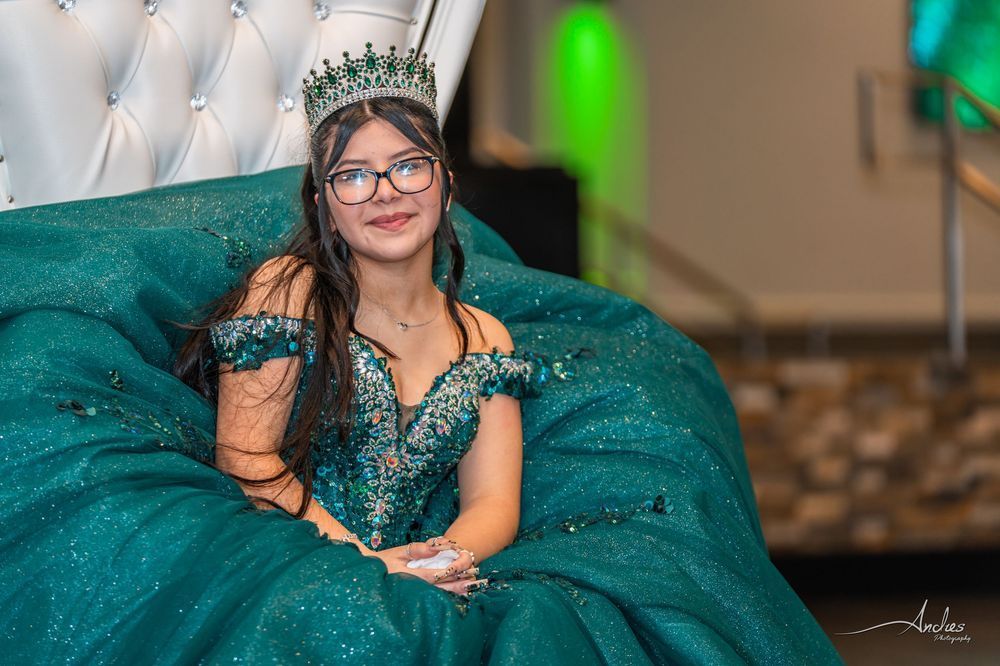 Young person in a teal gown and crown, seated on a matching sofa at an elegant event