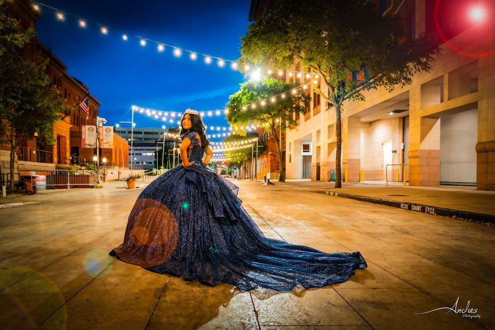 Woman in a dark blue gown on a lit city street at night