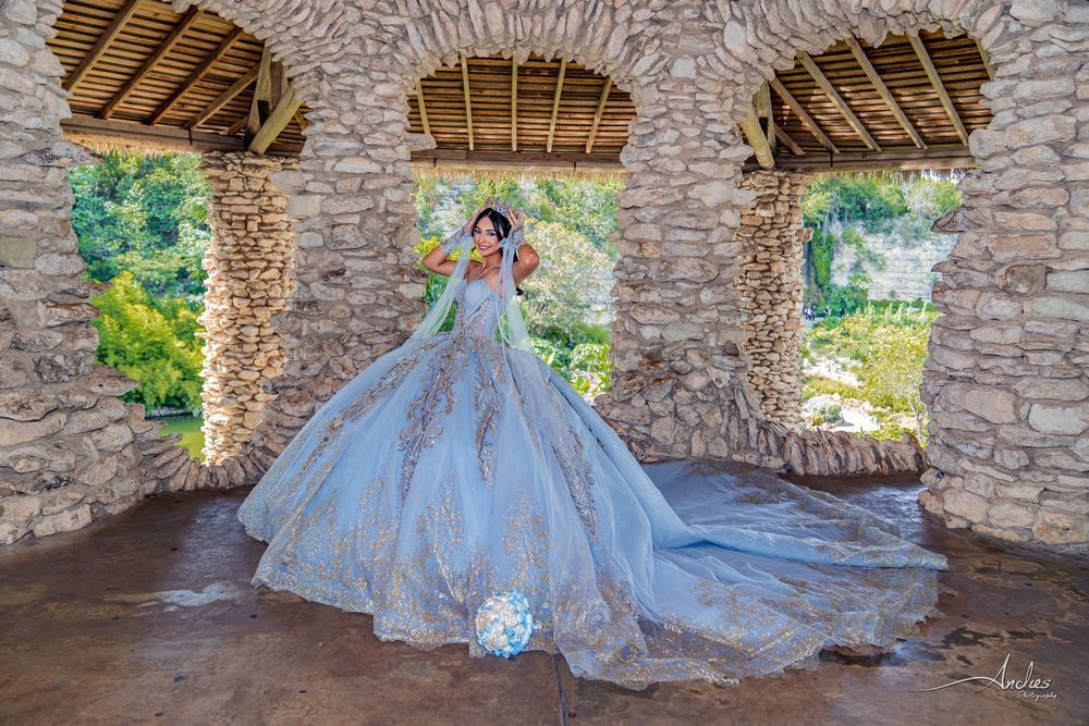 Bride in a flowing blue gown standing in a stone pavilion with arched openings and a long train