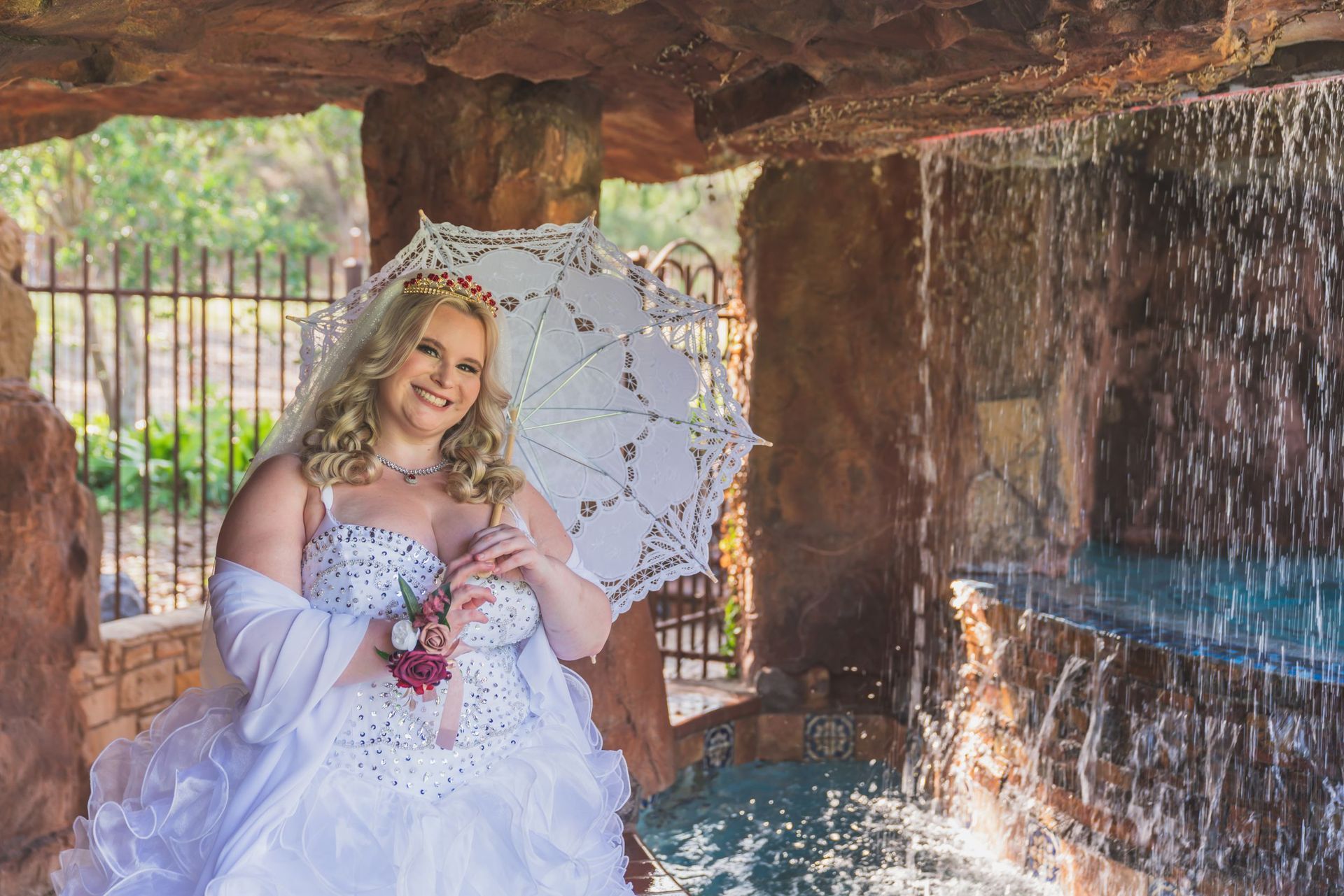 Woman in a white dress holding a lace parasol beside a waterfall in a rocky grotto