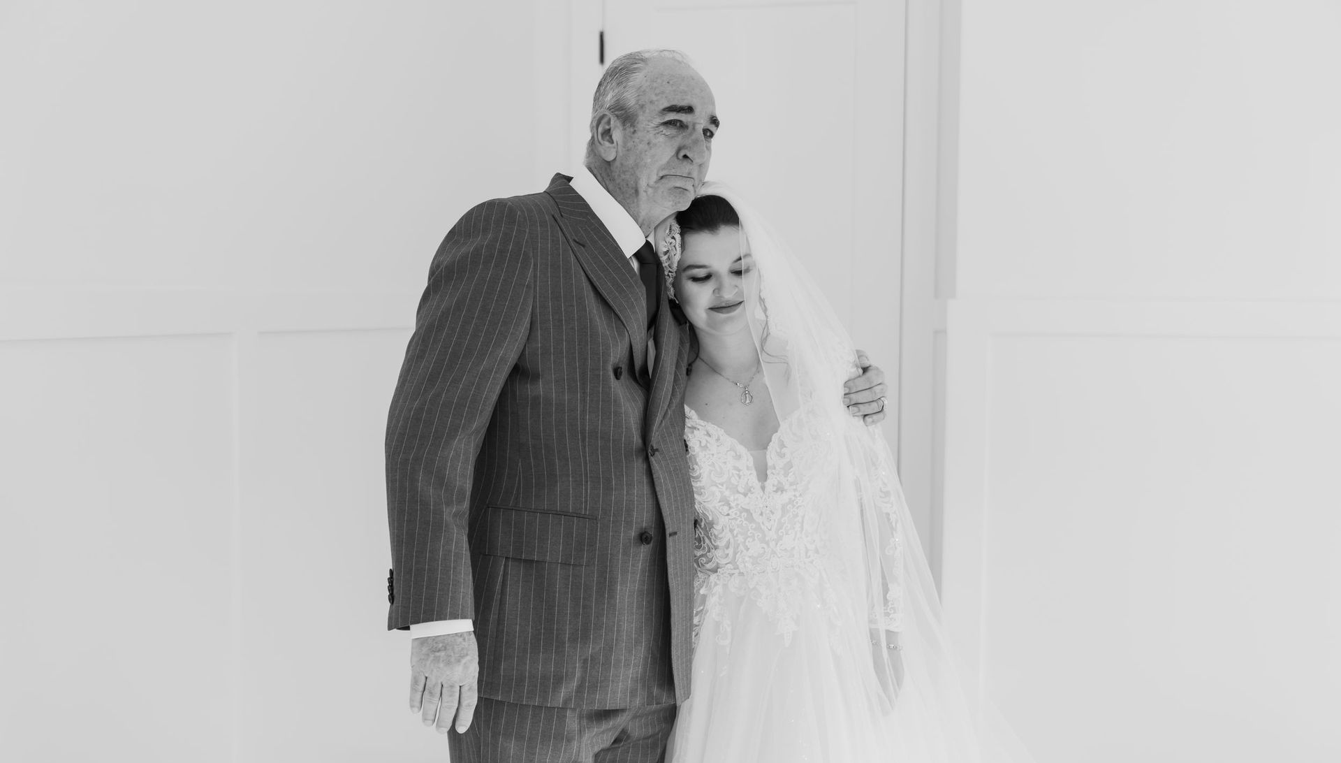 Bride and groom embracing in a bright white room, both dressed in formal wedding attire