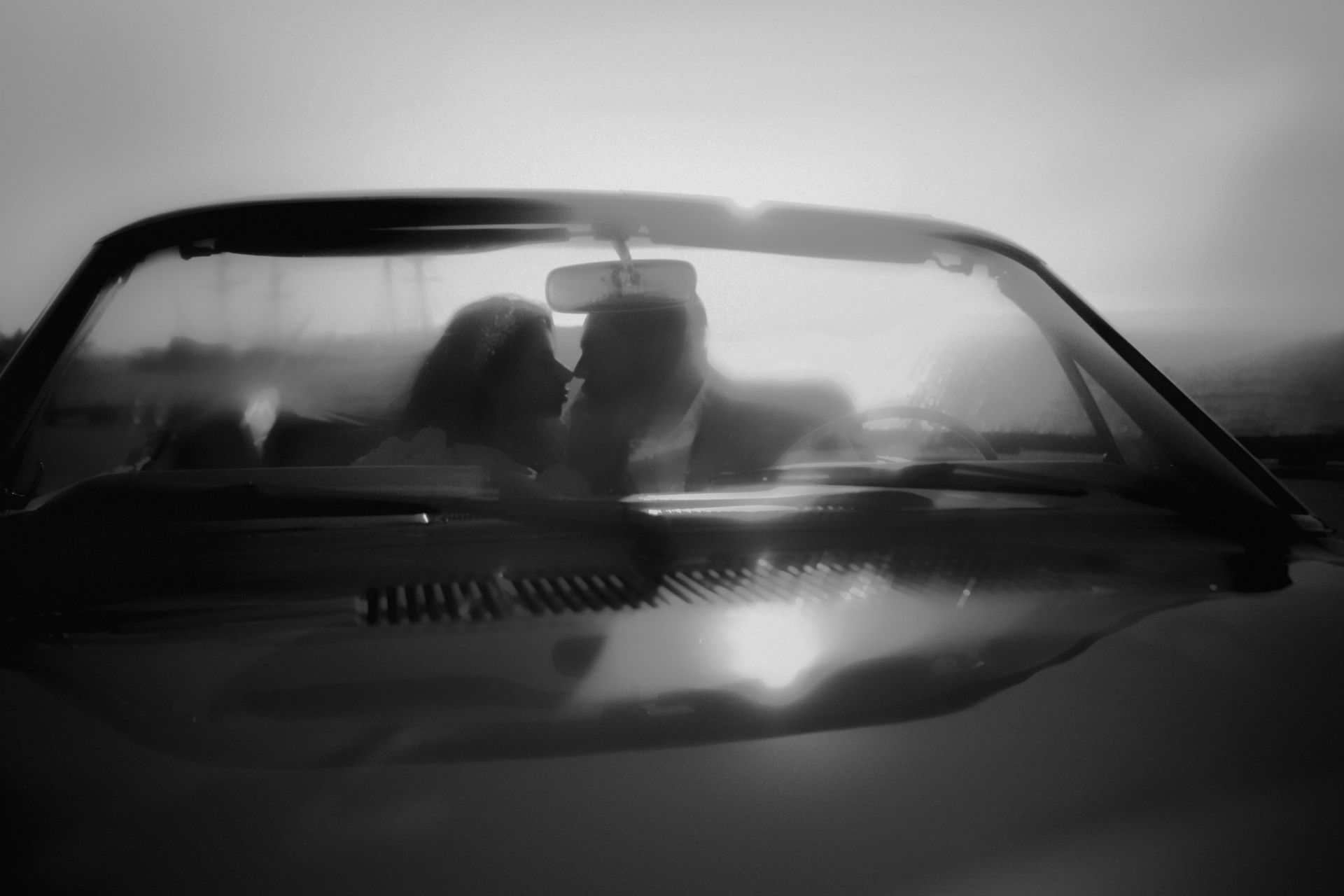 Two silhouetted people in a car at night, seen through the windshield with bright glare.