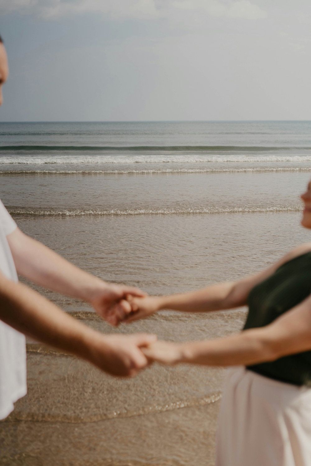 Two people holding hands on a beach, with calm ocean waves in the background