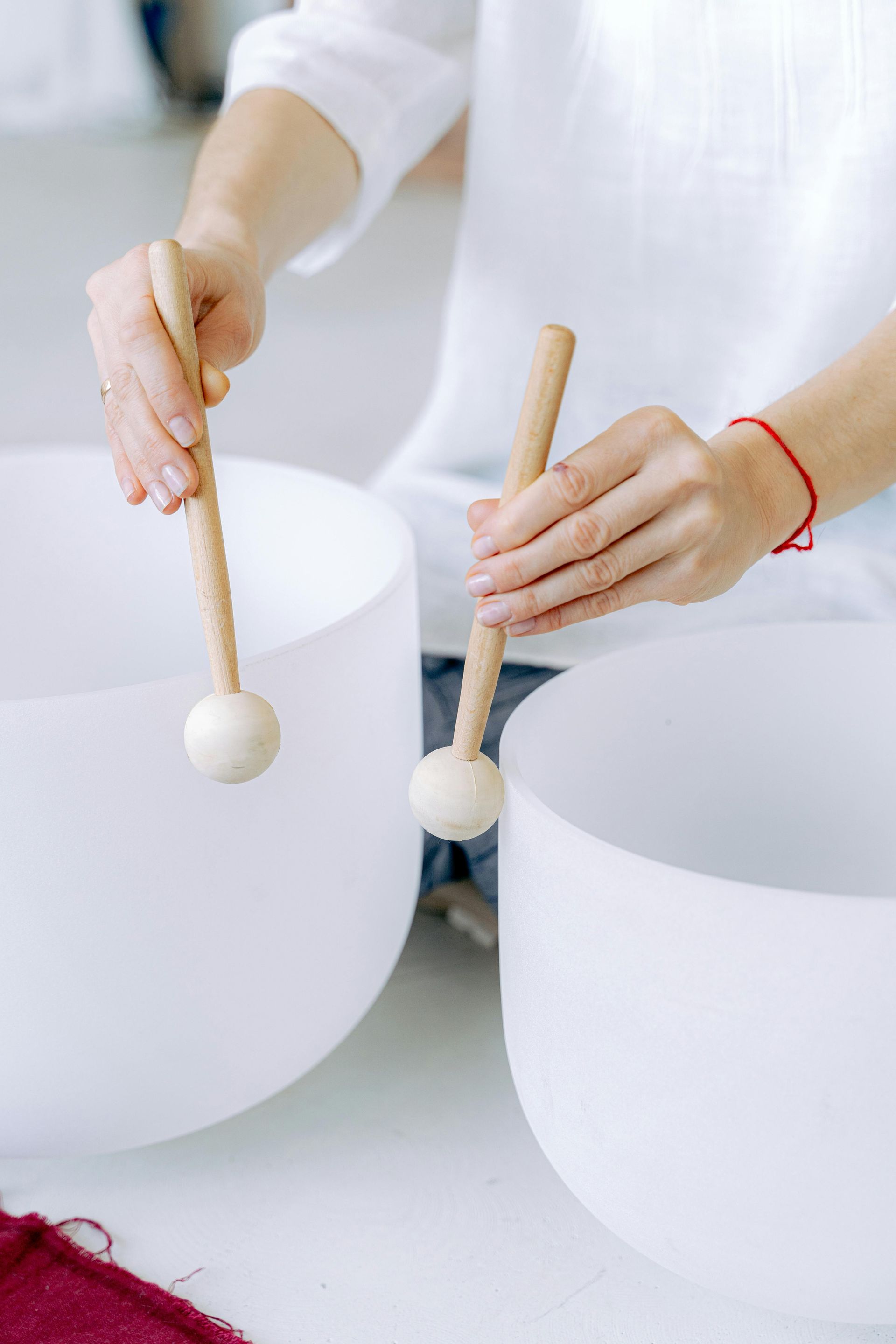 Hands playing two white crystal singing bowls with wooden mallets.