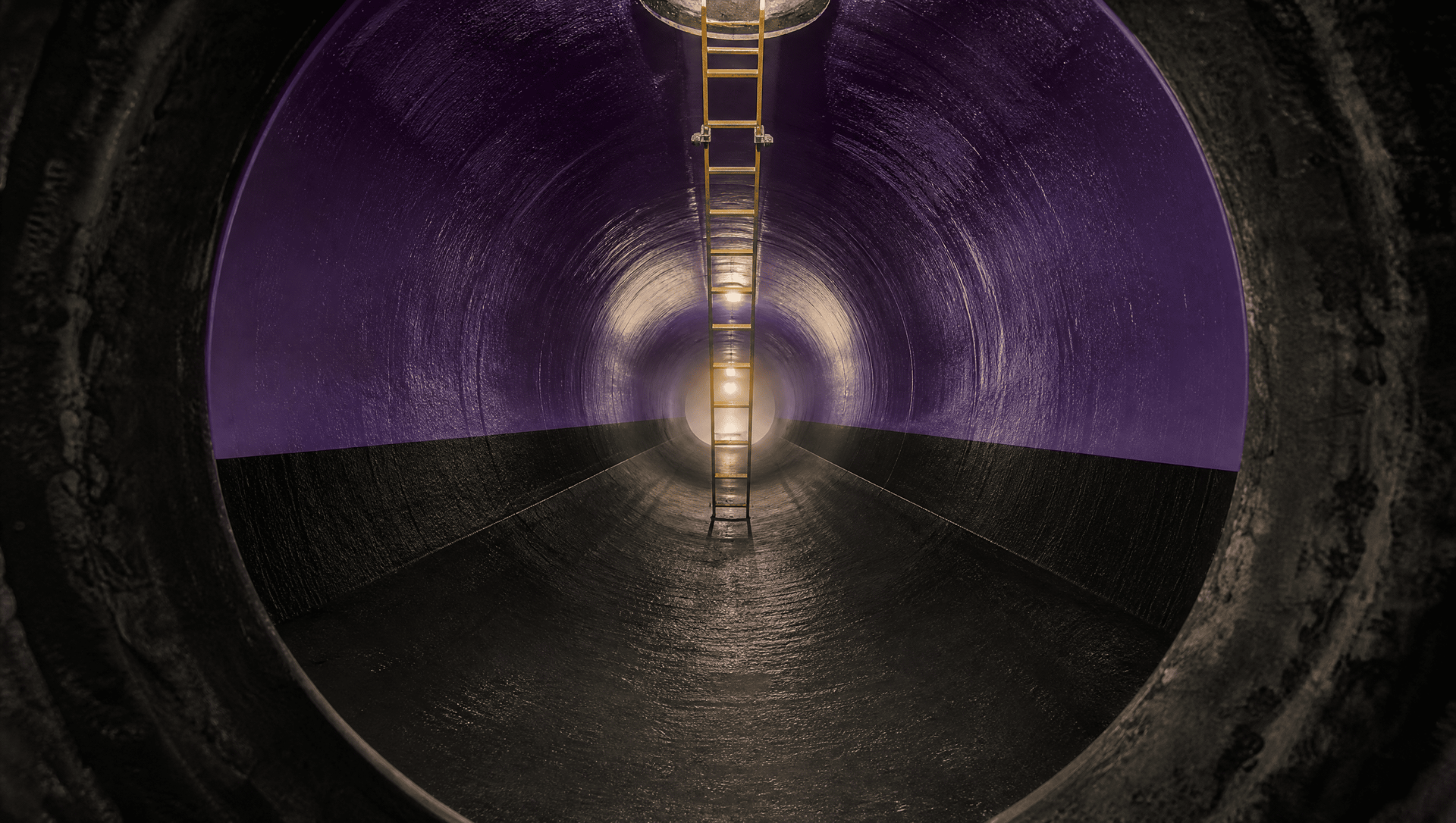 Um túnel circular escuro com paredes roxas e uma luz brilhante no fundo, visto de dentro.