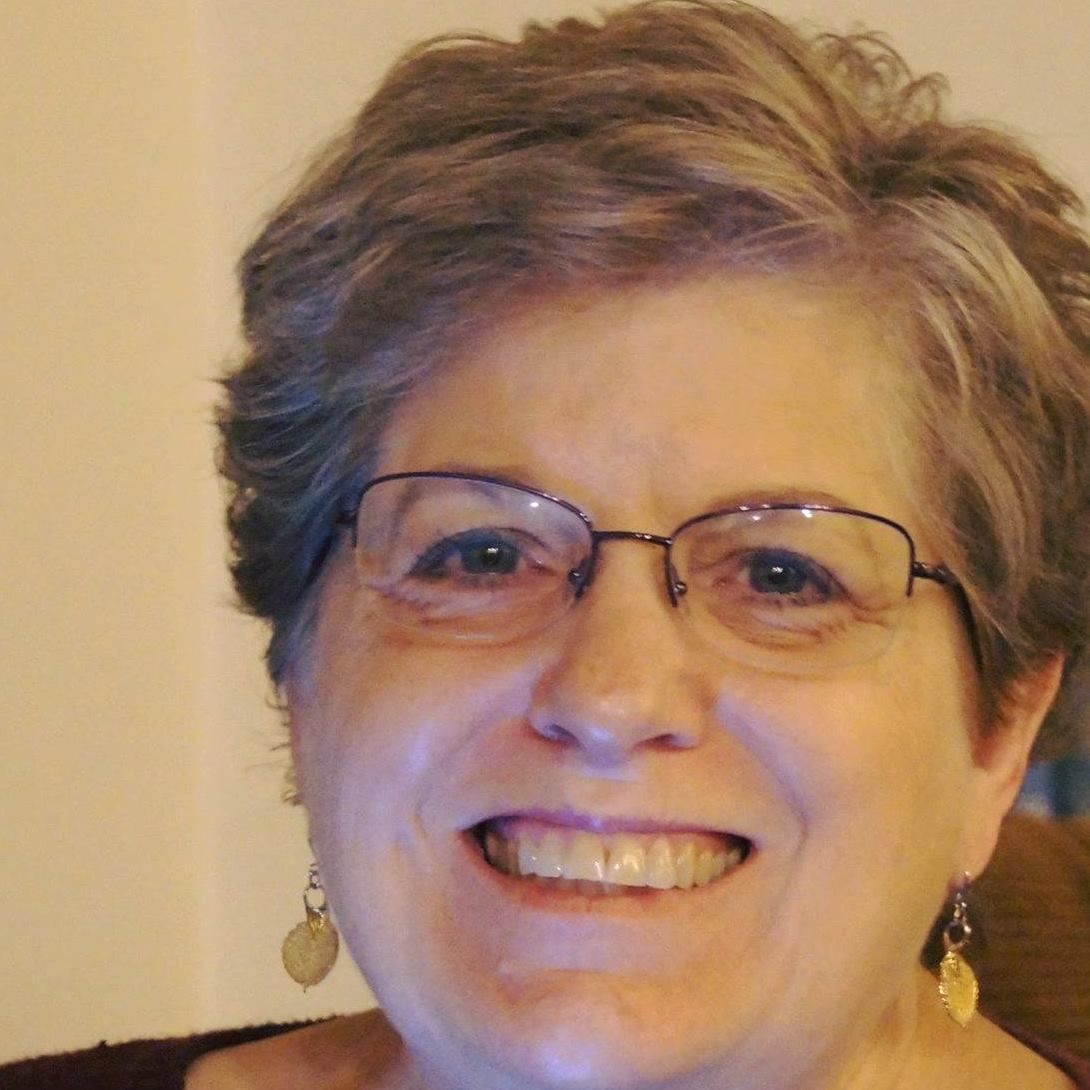 A woman wearing glasses and earrings is smiling for the camera.