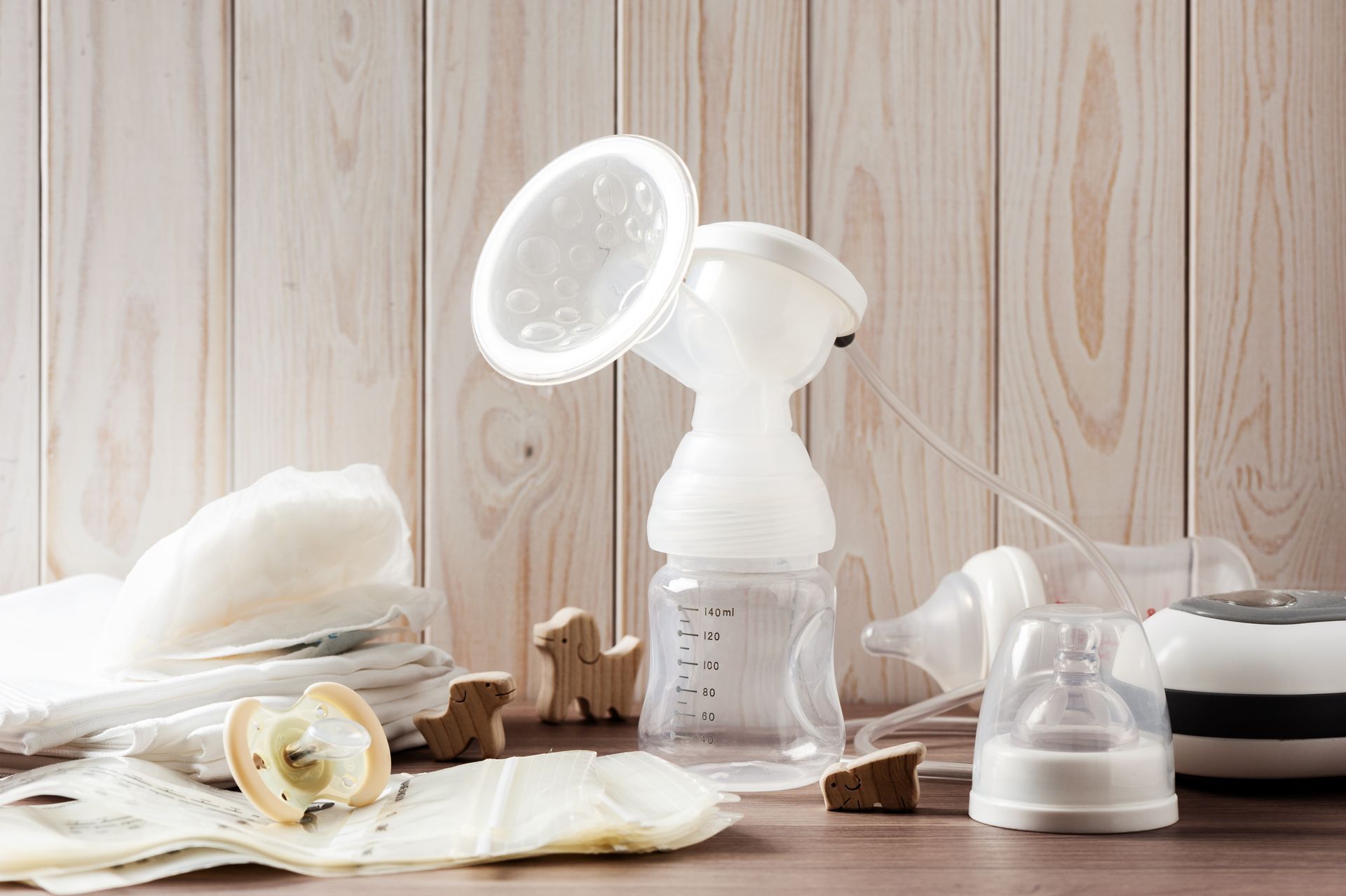 A breast pump is sitting on a wooden table next to a pacifier.