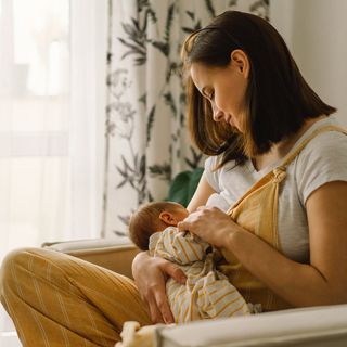 A woman is breastfeeding her baby while sitting on a couch.