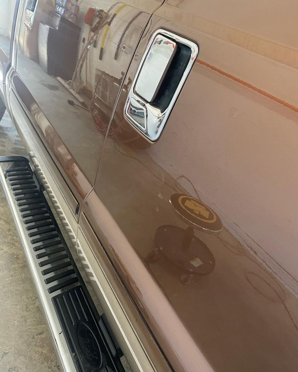 Side view of a brown truck with chrome door handles and a black running board along the lower edge