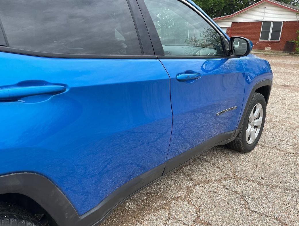Blue SUV parked on gravel beside a red house on a cloudy day