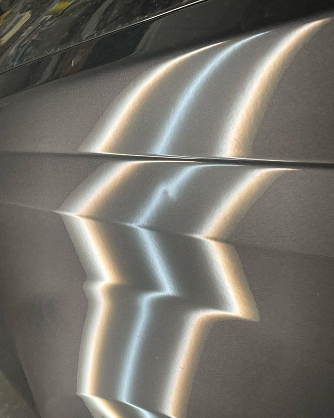Close-up of a metallic car door with bright reflections and zigzag light streaks