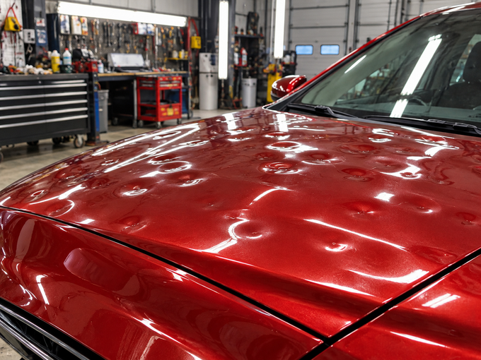 Close-up of a red car hood and chrome grille under bright garage lights